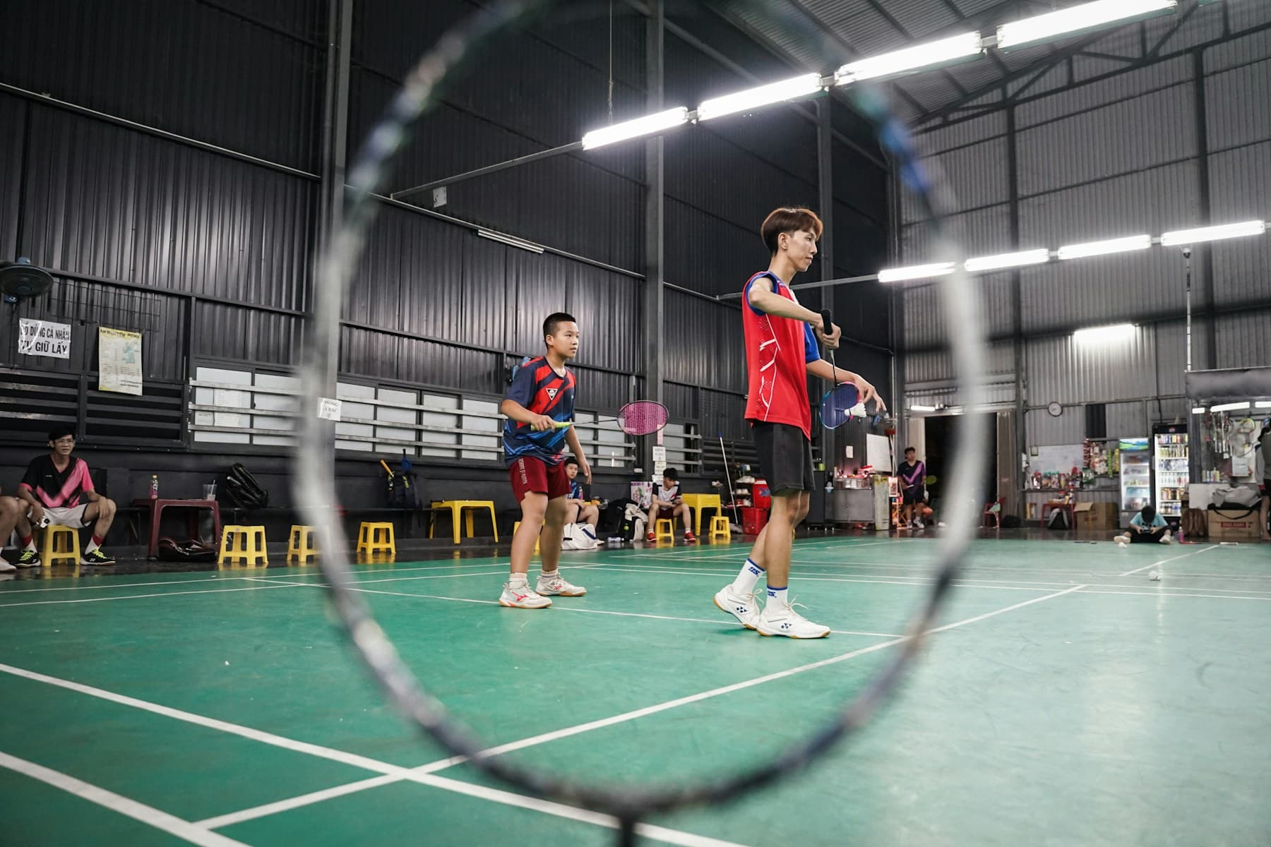 Badminton players preparing to serve on an indoor court